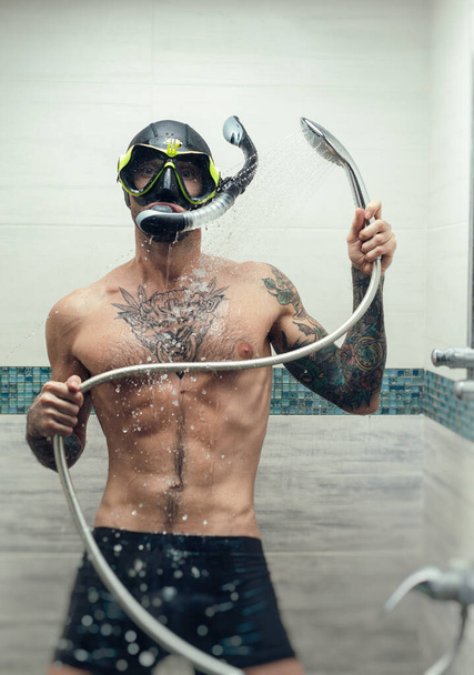 un hombre con una máscara de buceo en la ducha se rocía con agua - Foto, imagen