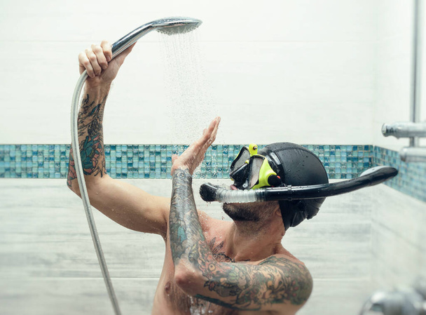 un homme portant un masque de plongée sous la douche est arrosé d'eau - Photo, image