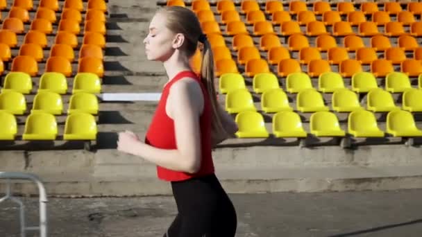 ajuste caucásico bonita mujer en ropa deportiva corre a lo largo de statium tribune al aire libre - Imágenes, Vídeo