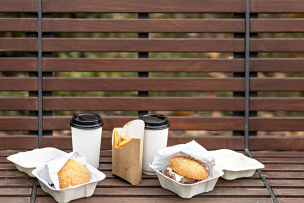 Szybkie żarcie. Papierowe kubki z kawą, pudełkami po hamburgerach i frytkami na parkowym bench.Takeaway food concept. - Zdjęcie, obraz