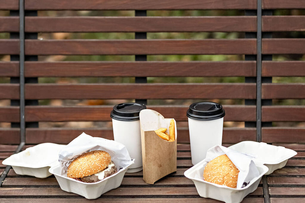 Fast food. Kahve bardakları, hamburger kutuları ve kızartmalar park bankında. Paket yemek kavramı.. - Fotoğraf, Görsel