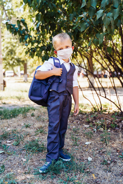 Coronavirus and new rules for staying at school. An elementary school student goes to school in the morning. Always wear a protective medical mask. Looks smart and neat in a new uniform. Covid-19. - Photo, Image