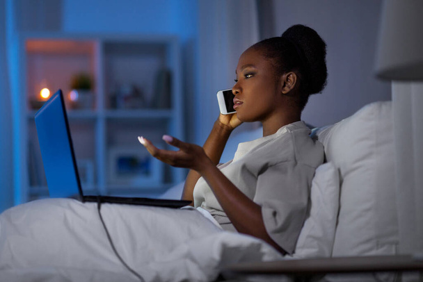 woman with laptop calling on smartphone in bed - Valokuva, kuva