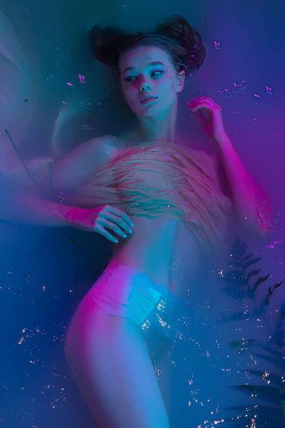 Portrait of young beautiful adorable girl posing in water in modern neon light. - Fotó, kép
