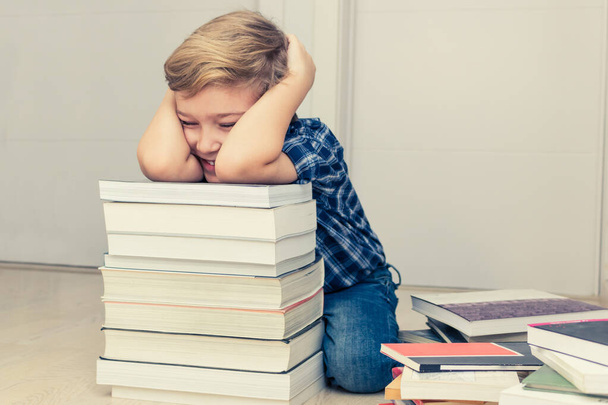 Счастливый малыш веселится среди стопки книг, пока учится дома.  - Фото, изображение
