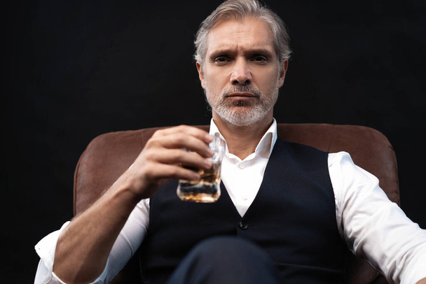 Portrait of handsome elegant mature man with a glass whiskey in a dark room. - Fotó, kép