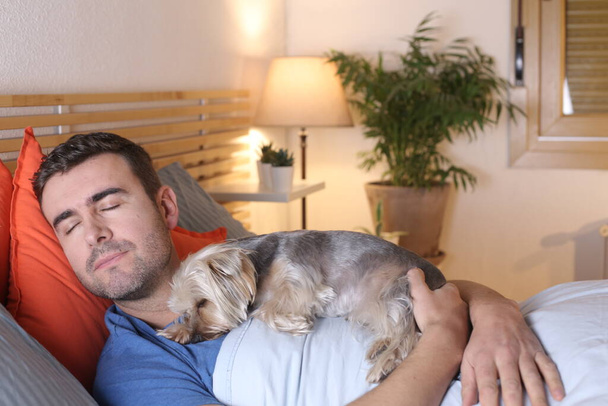 красивый молодой человек со своей собакой отдыхает в постели дома - Фото, изображение