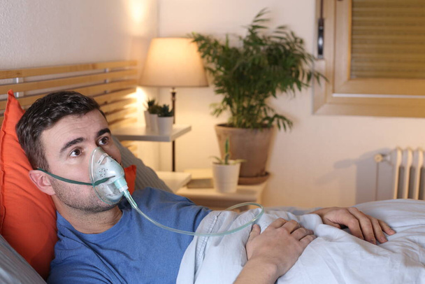jovem bonito com máscara de oxigênio medicinal na cama em casa - Foto, Imagem