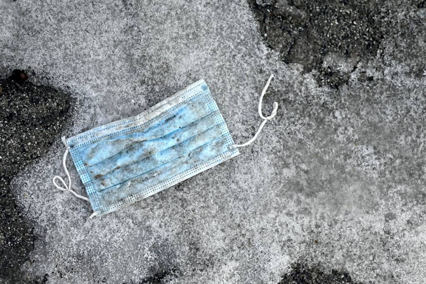 Brudna maska medyczna porzucona na pokrytym lodem chodniku. - Zdjęcie, obraz