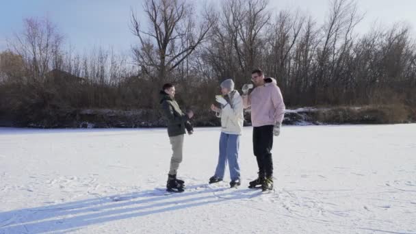 Νέοι ευτυχισμένοι φίλοι πίνουν ένα ζεστό τσάι και τρώει σνακ μετά βόλτες παγοδρομία στην παγωμένη λίμνη στο δάσος - Πλάνα, βίντεο