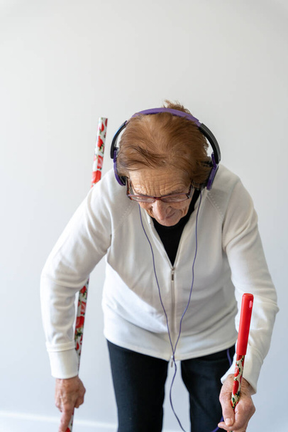 Allegro 90 anni femmina godendo la musica in cuffia mentre spazzare pavimento con scopa e fare i lavori di casa - Foto, immagini