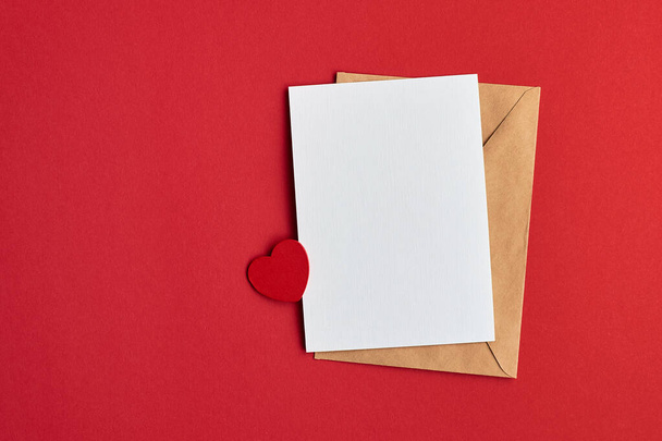 Tarjeta de San Valentín maqueta con sobre y pequeño corazón sobre fondo de papel rojo, vista superior, espacio para copiar - Foto, imagen