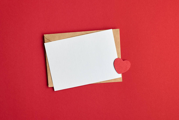 Valentines day card mockup with envelope and small heart on red paper background, top view, copy space - Zdjęcie, obraz