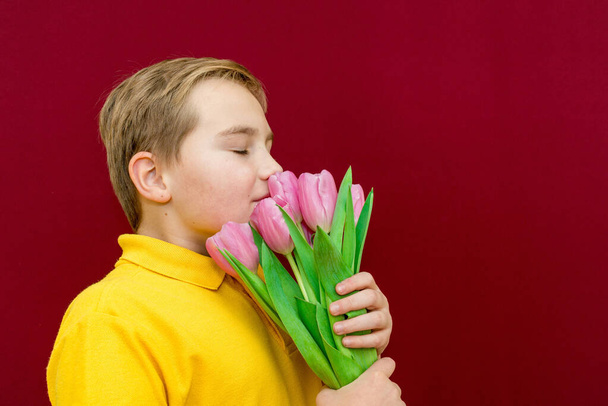 A happy son boy snuff tulips on red studio background.Boy is closed eyes.Side view image. - Foto, Imagem