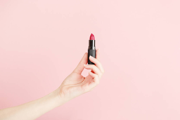 Female hand holding lipstick. Equipment for maquillage. Make-up and visagist. Place for text or creative design. Mockup style. Cosmetic and beauty concept. Isolated on pink. - Photo, Image