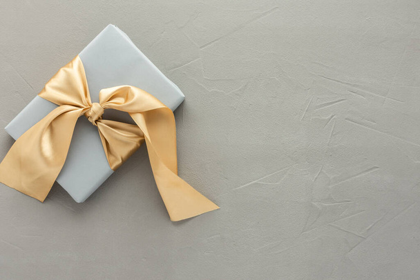 Caja de regalo gris con lazo dorado sobre un fondo de hormigón gris, concepto de cumpleaños o San Valentín, vista superior, espacio para copiar - Foto, Imagen