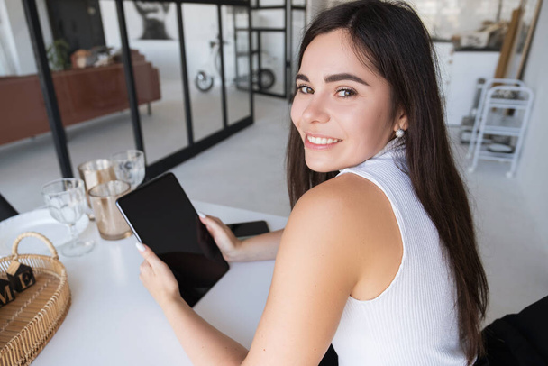 Brunette Kaukasische vrouw in witte blouse en zwarte rok werkt via internet met behulp van tablet. Werk vanuit huis concept. Ruimte voor tekst. - Foto, afbeelding