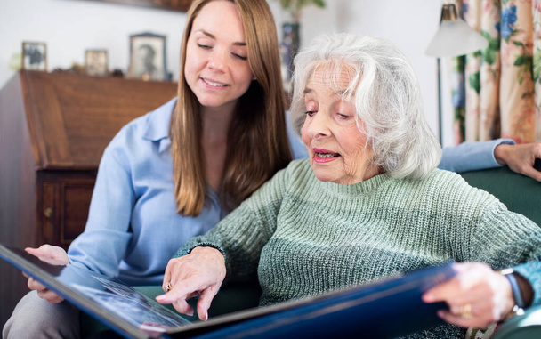 Grandmother Looking At Photo Album With Adult Granddaughter At Home - Photo, Image