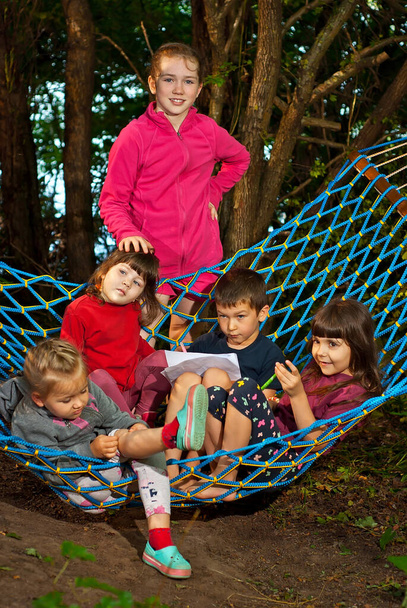 Children sit in a hammock. Boy and girl play in nature in summer. Children's entertainment in the garden. - Photo, Image