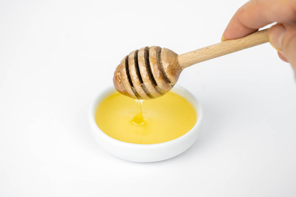 Liquid honey pouring with wooden stick in small white plate - Valokuva, kuva