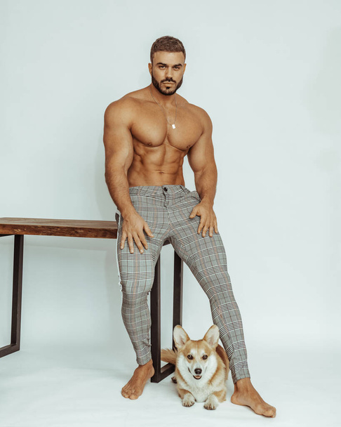 Shirless sexy man met corgi hond op tafel. Stijlvolle knappe bink met hond in studio. - Foto, afbeelding