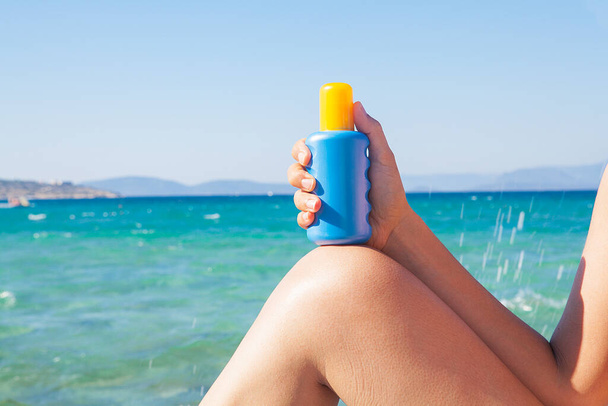Žena drží opalovací krém v ruce. Slunečný den a na pláži. Modré moře v pozadí. Koncept relaxace. - Fotografie, Obrázek