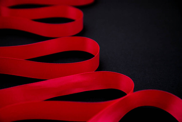 A red satin ribbon lies on a black background. Minimalistic photography.The ribbon twists beautifully. Gift wrapping. The concept of March 8 and Valentine's Day. - Zdjęcie, obraz