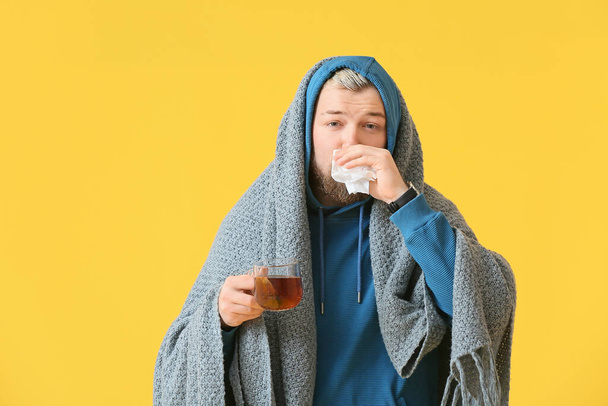 Sick young man with hot tea on color background - Photo, Image