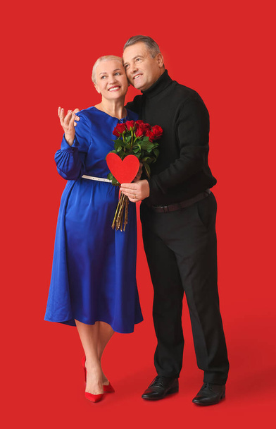 Зрелая пара с сердцем и цветами на цветном фоне. Празднование Дня Святого Валентина - Фото, изображение