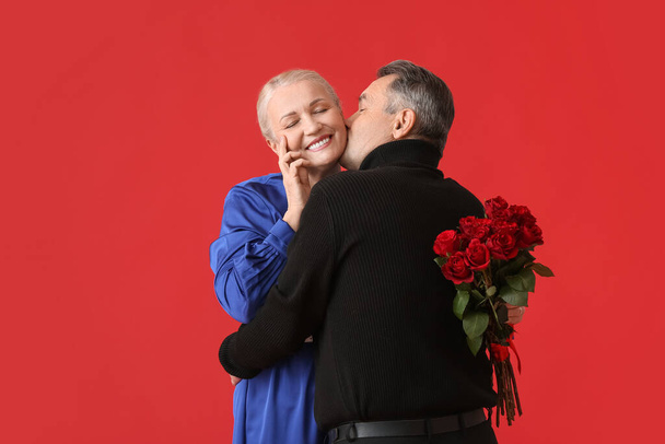 Mature man greeting his wife on Valentine's Day against color background - Photo, Image