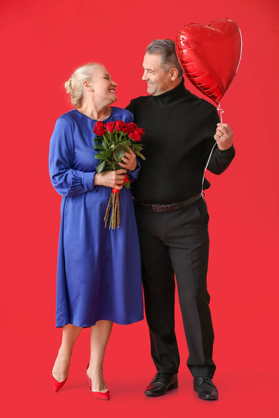 Mature couple with balloon and flowers on color background. Valentine's Day celebration - 写真・画像