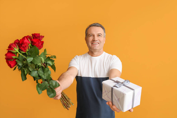 Mature man with bouquet of beautiful flowers and gift on color background - Photo, Image