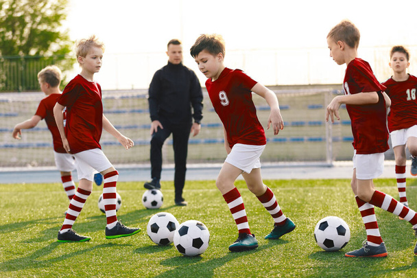 Boys in Soccer Jersey Kits Kicking Soccer Balls on Training Session. Young Football Coach Teaching School Kids. Children Running Balls on Grass Stadium on a Sunny Day - Foto, imagen