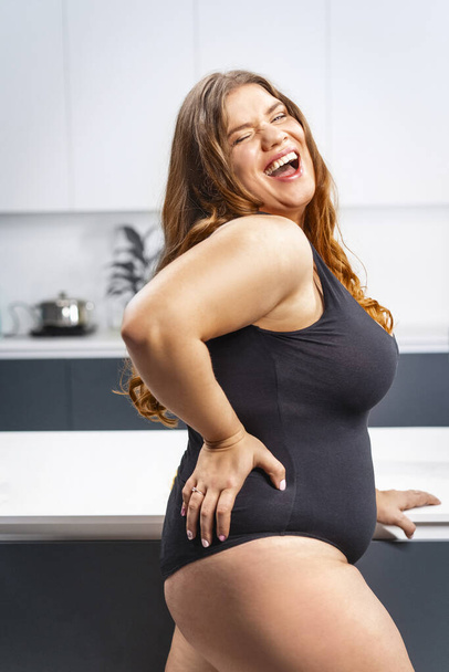 Young fat woman trying diet. Girl standing next to the kitchen table. Diet young fat woman standing on kitchen. Close up chubby female lowering BMI weight. Trying to loose weight fast - Zdjęcie, obraz