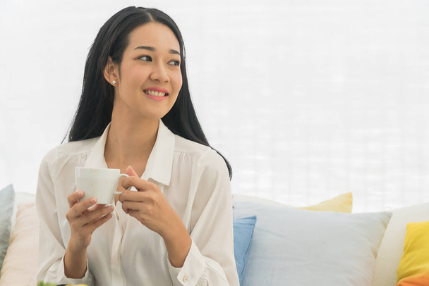 Schöne asiatische junge Frau sitzt mit einer weißen Tasse Kaffee zu Hause. - Foto, Bild