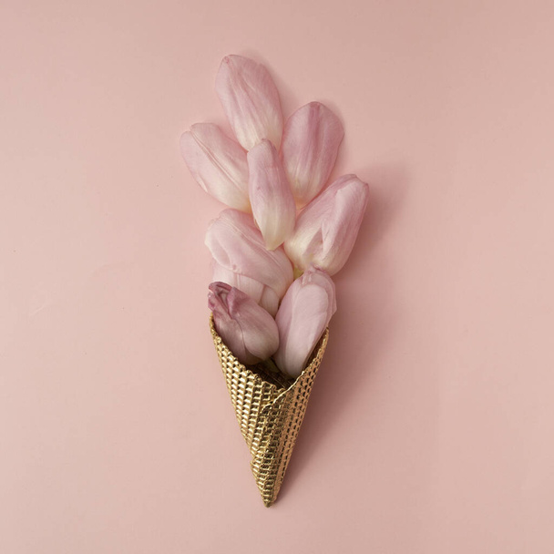 Gouden ijskegel gevuld met roze tulpenblaadjes op bleke roos bacground. Ik hou van esthetiek. Creatief concept. - Foto, afbeelding