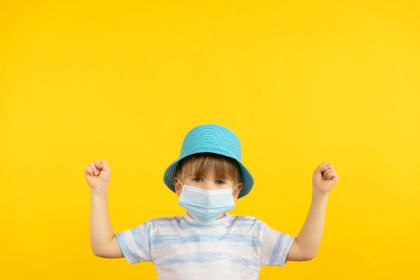 Happy child dreaming about vacation. Portrait of kid wearing protective mask indoor. Summer holiday during coronavirus COVID-19 pandemic concept. - 写真・画像