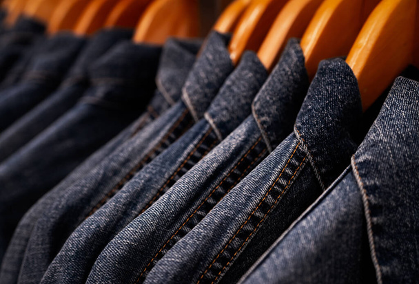洋服屋のラックに掛けられたジャケットジーンズに焦点を当てました。デニムジーンズのパターンを持つジーンズ。繊維産業。ジーンズファッションとショッピングのコンセプト。服のコンセプト。デニムジャケット販売のためラック. - 写真・画像
