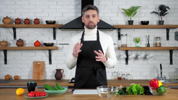 Чоловік шеф-кухар в чорному фартусі розповідає вчить онлайн відео кулінарний вебінар на кухні
 - Кадри, відео