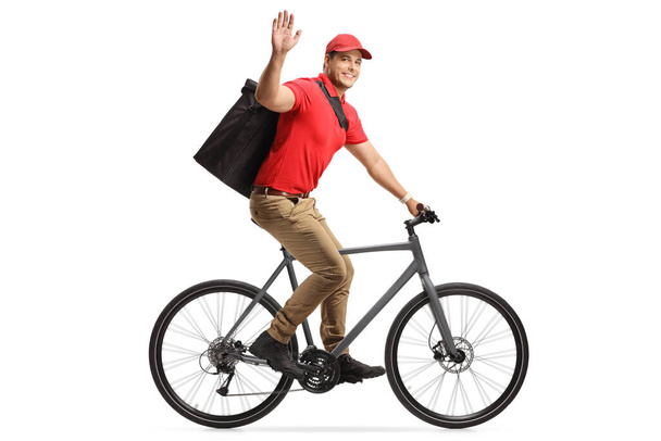 Food delivery man in a red t-shirt delivering food with a bicycle and greeting with hand isolated on white background - Foto, Imagem