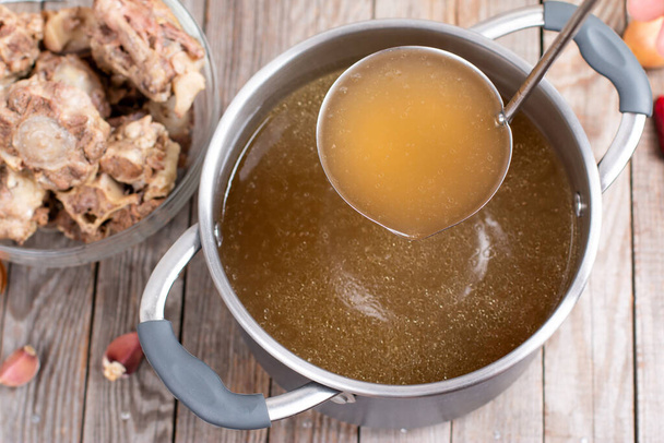 Saucepan with bouillon with a ladle on the table. Bone broth - Photo, Image