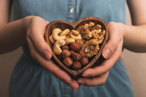 Woman holding heart shaped plate with mixed nuts. Healthy organic food. Close up - Photo, Image