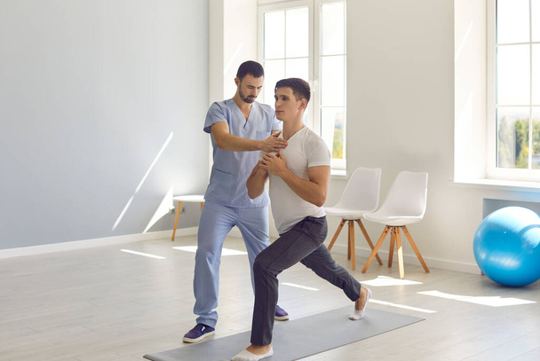 Osteopath fixing and controlling man patients movements during exercising on fitness mat - Φωτογραφία, εικόνα
