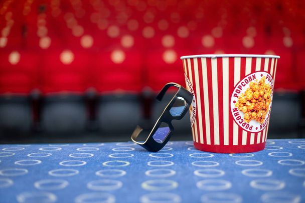 A large bucket of popcorn and 3D glasses on the background of cinema chairs - Φωτογραφία, εικόνα