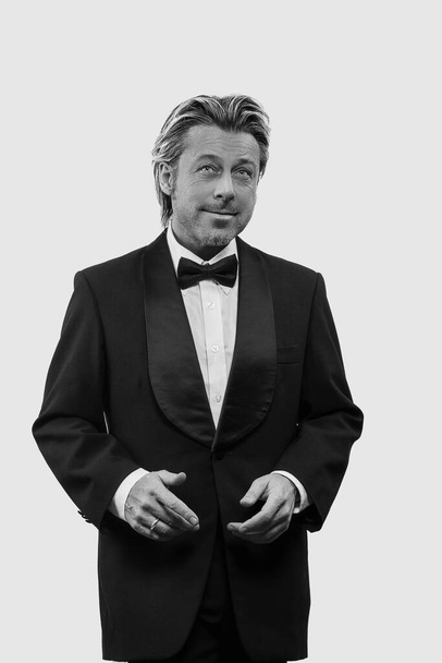Funny man in tuxedo in front of white wall. Black and white photo. - 写真・画像