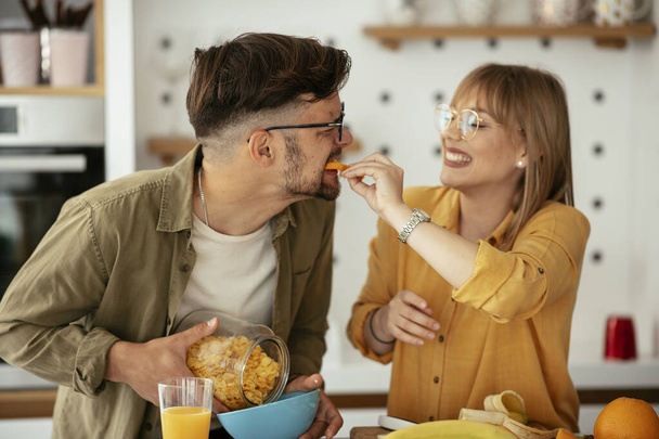 Genç çift evde kahvaltı hazırlıyor. Sevgi dolu çift mutfakta mısır gevreği yiyor.. - Fotoğraf, Görsel