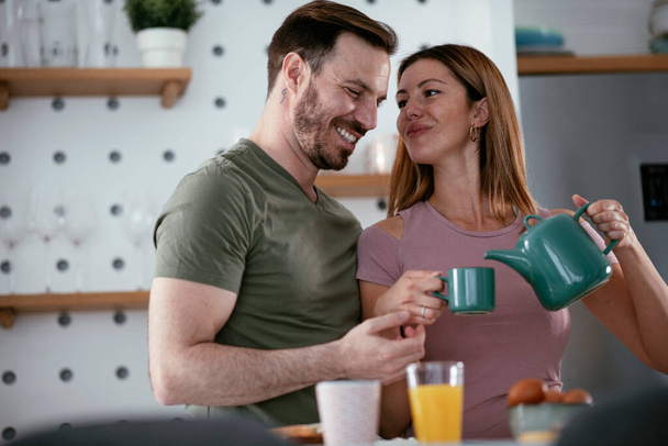 Amar pareja bebiendo café mientras se prepara el desayuno. - Foto, Imagen
