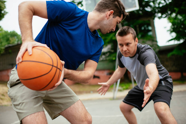 Dos jóvenes jugando baloncesto en el parque. Amigos teniendo un partido amistoso al aire libre - Foto, Imagen