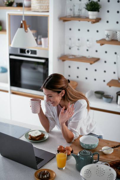 Mujer joven disfrutando de su desayuno mientras trabaja en el portátil - Foto, Imagen