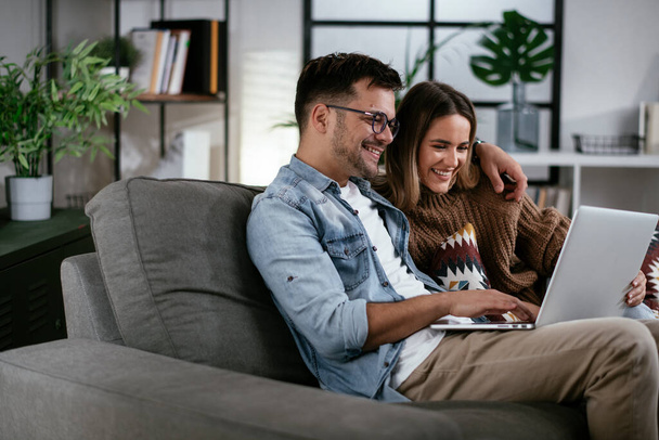 Ευτυχισμένο νεαρό ζευγάρι βλέποντας ταινία ή τηλεοπτική εκπομπή στο φορητό υπολογιστή στο σπίτι - Φωτογραφία, εικόνα